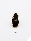 Black and gold map-shaped pin with Arabic text on a white background QATAR PRICE