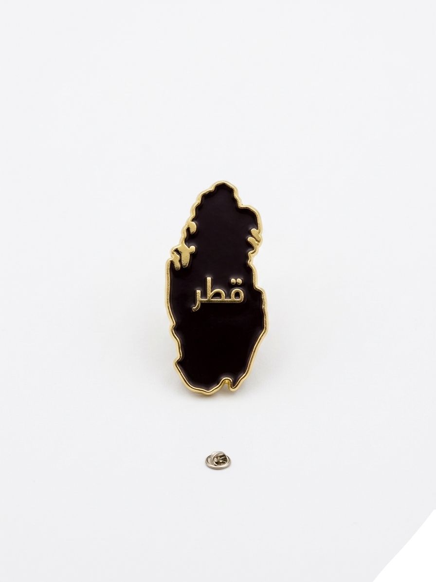 Black and gold map-shaped pin with Arabic text on a white background QATAR PRICE