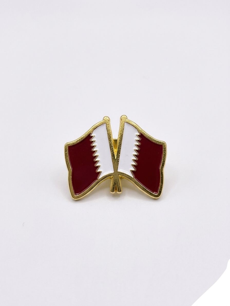 Two interlocking flags of Qatar on a gold pin against a white background